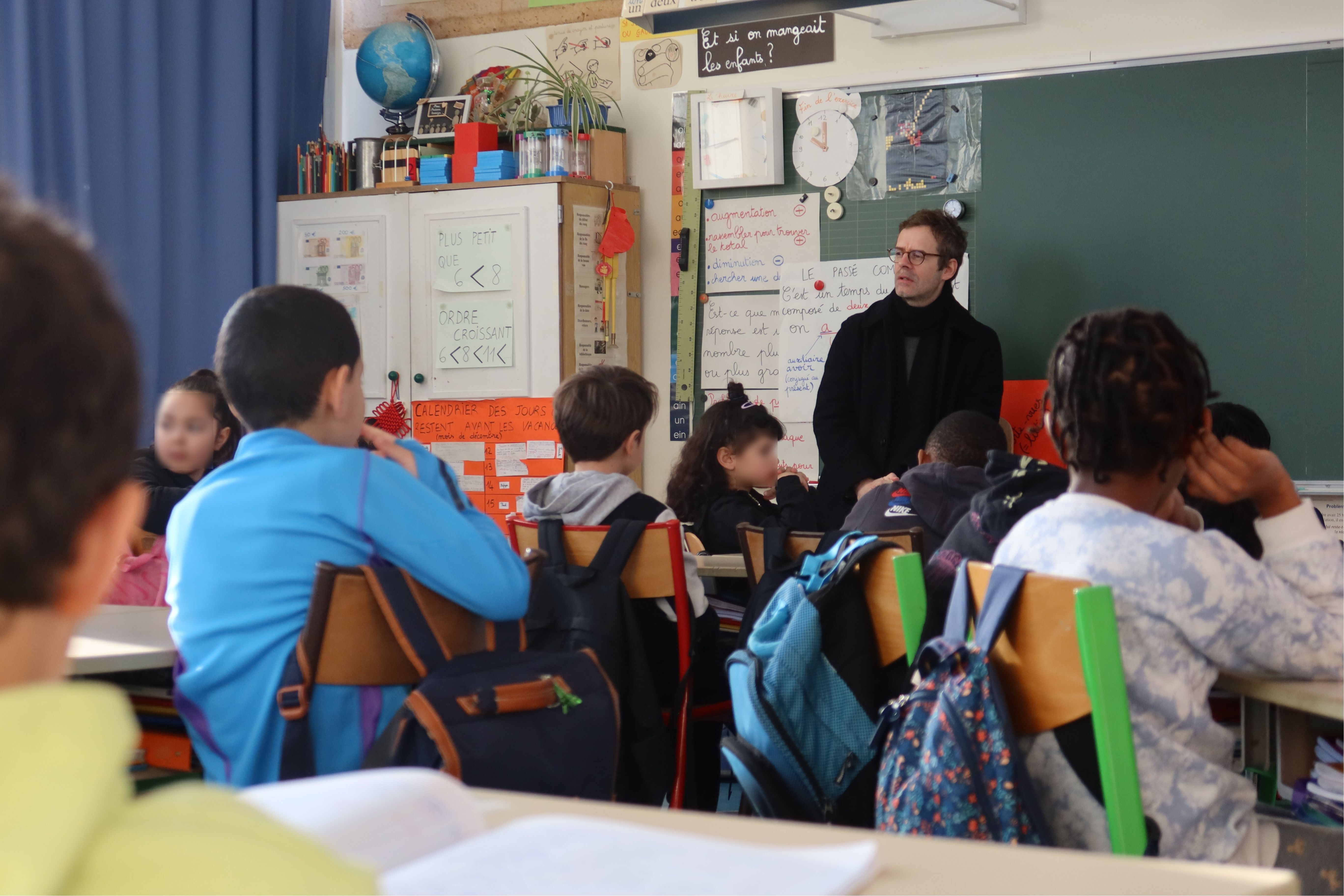 Les élèves sont assis à leur place en classe. Il écoute Armand Jalut qui leur parle.