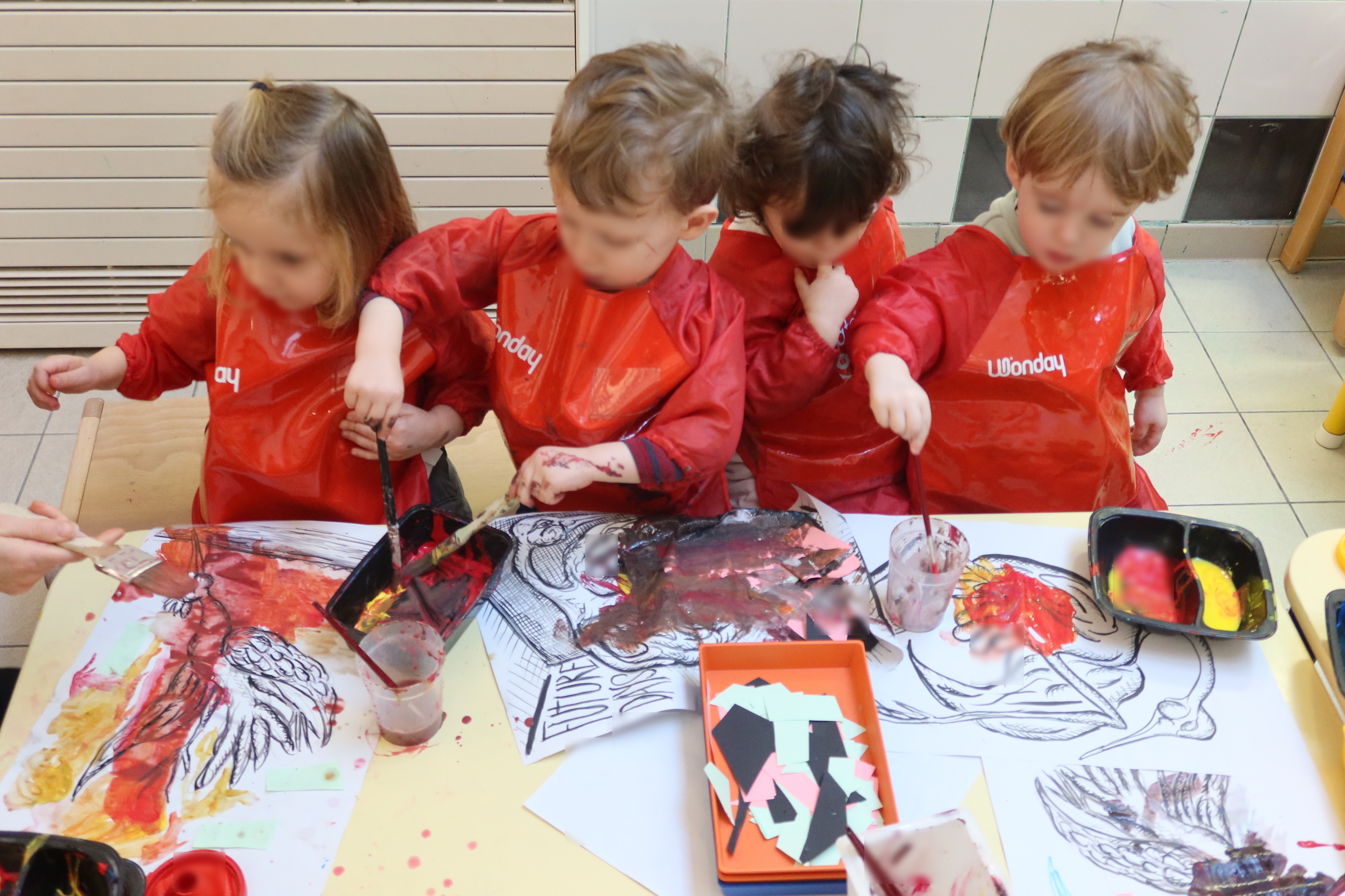 Quatre enfants assis en rang d'oignon peignent avec de gros pinceaux sur des dessins d'oiseaux.