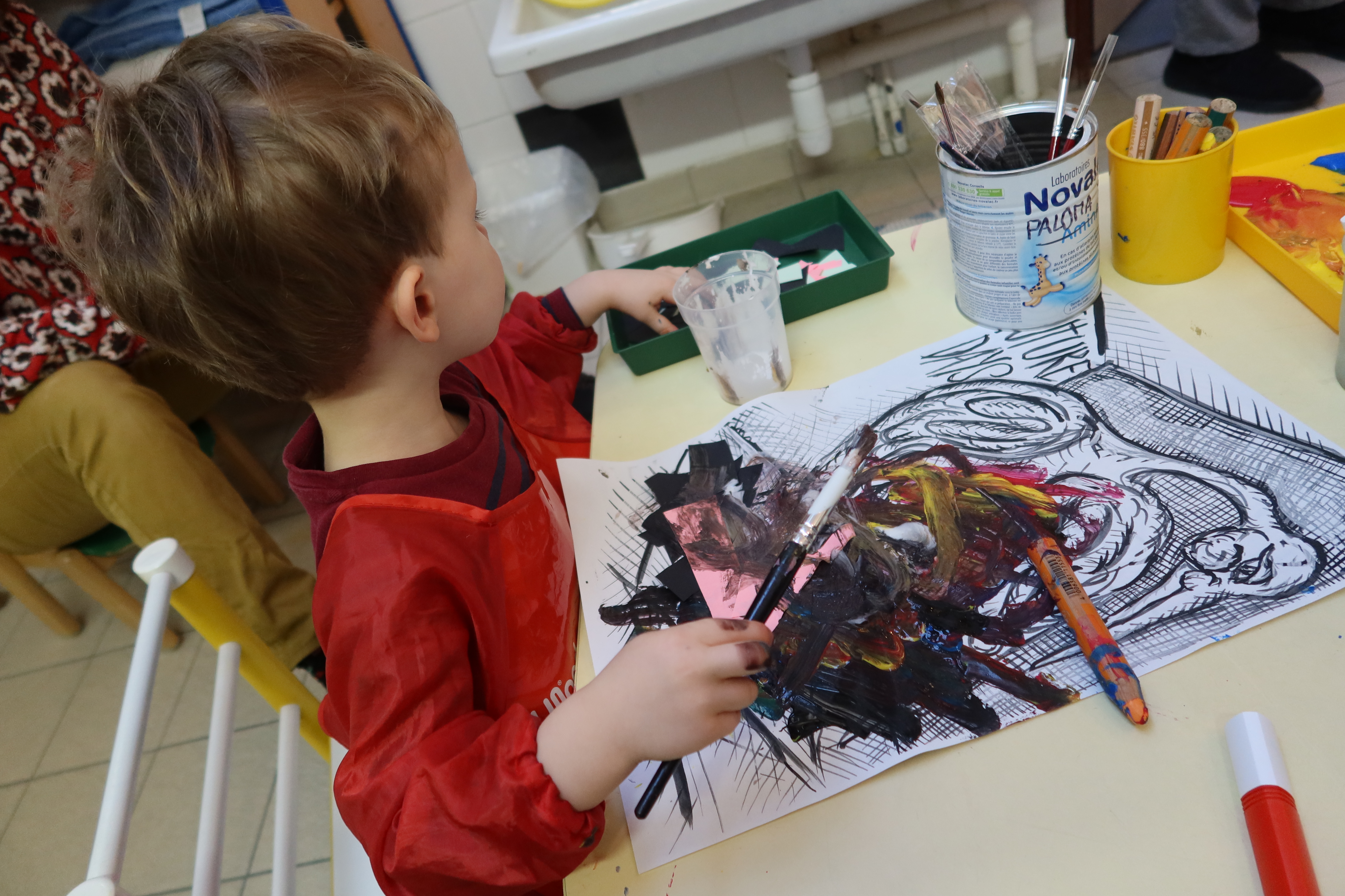 Un petit garçon place des petits bouts de papier colorés sur son dessin d'oiseau, puis il les recouvre de peinture