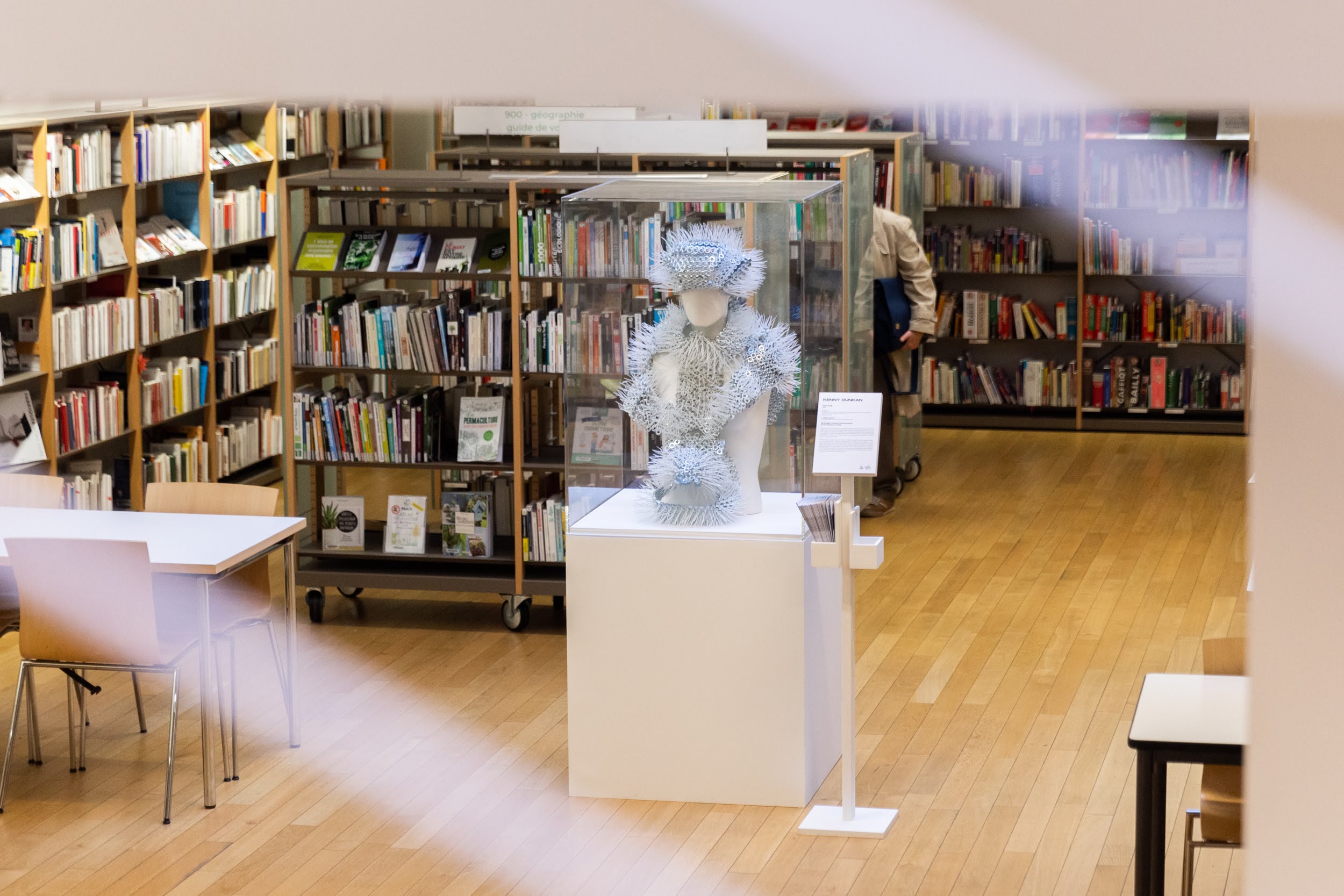 sculpture en écrou sur un mannequin posé sur un socle blanc dans une bibliothèque