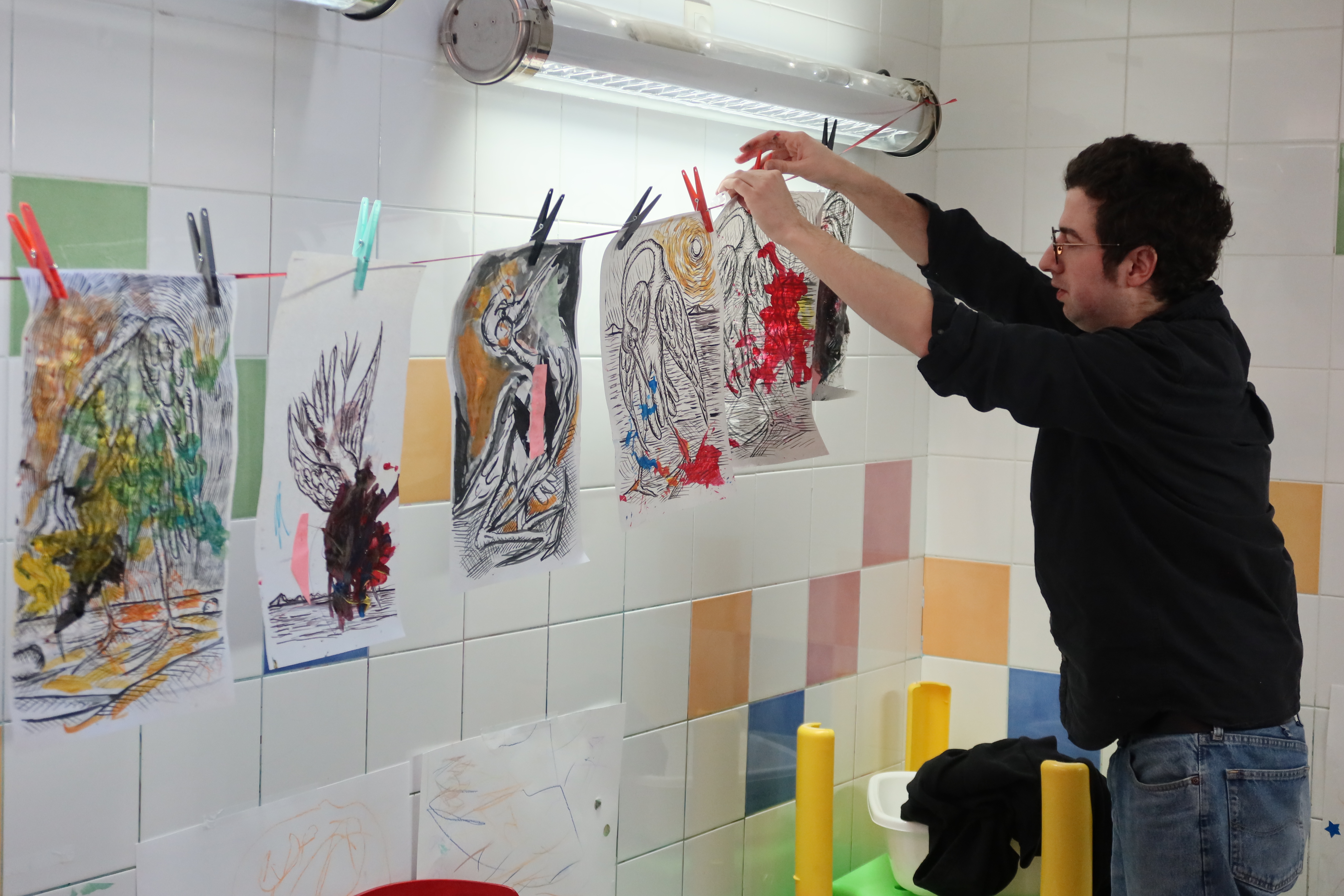Corentin Canesson accroche les peintures des enfants sur un fil avec des épingles à linge pour les faire sécher