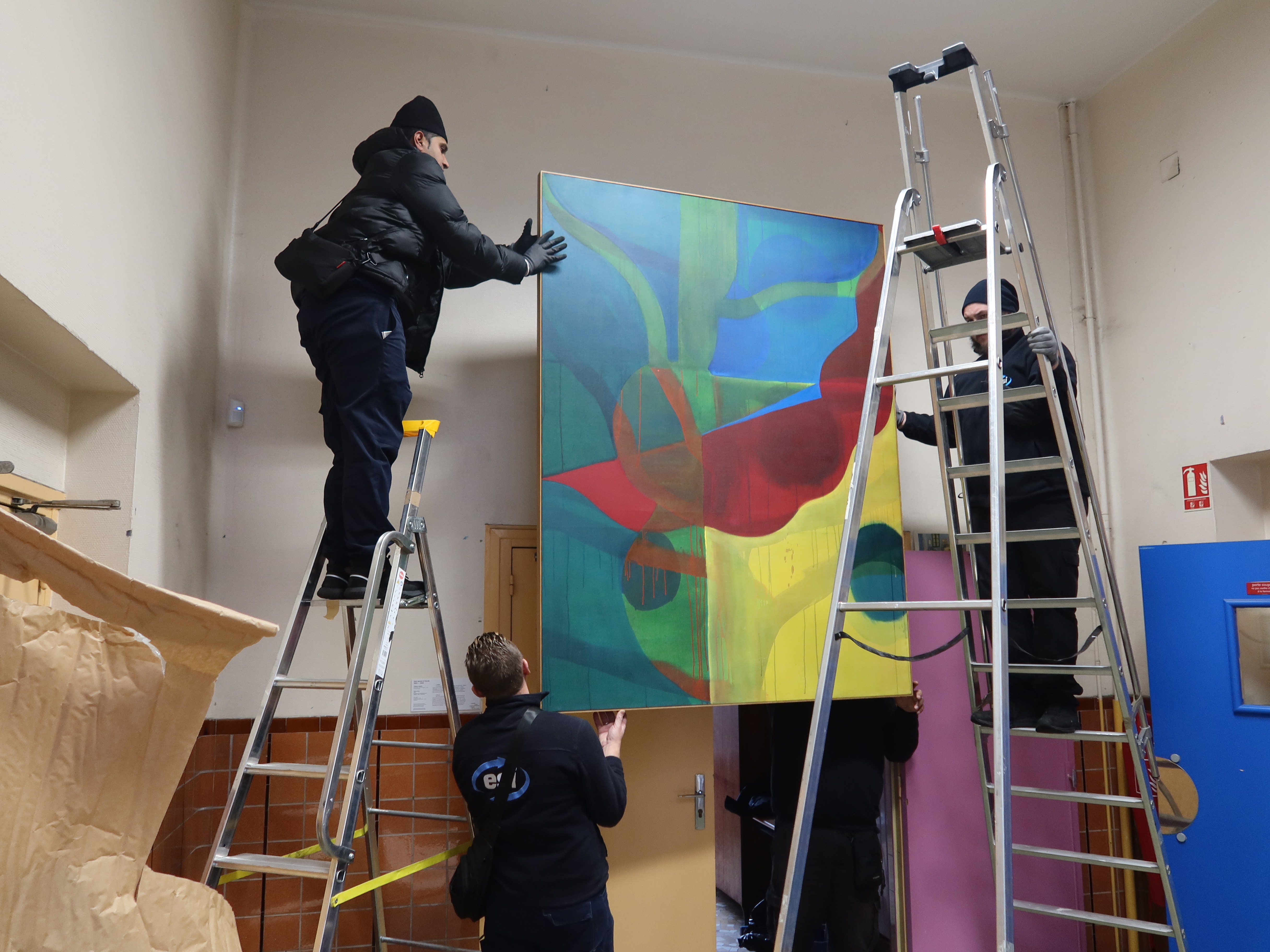 A l'école élémentaire Charles Hermite, quatre installateurs hissent sur deux escabeaux le tableau [Sans titre] de Gilgian Gelzer