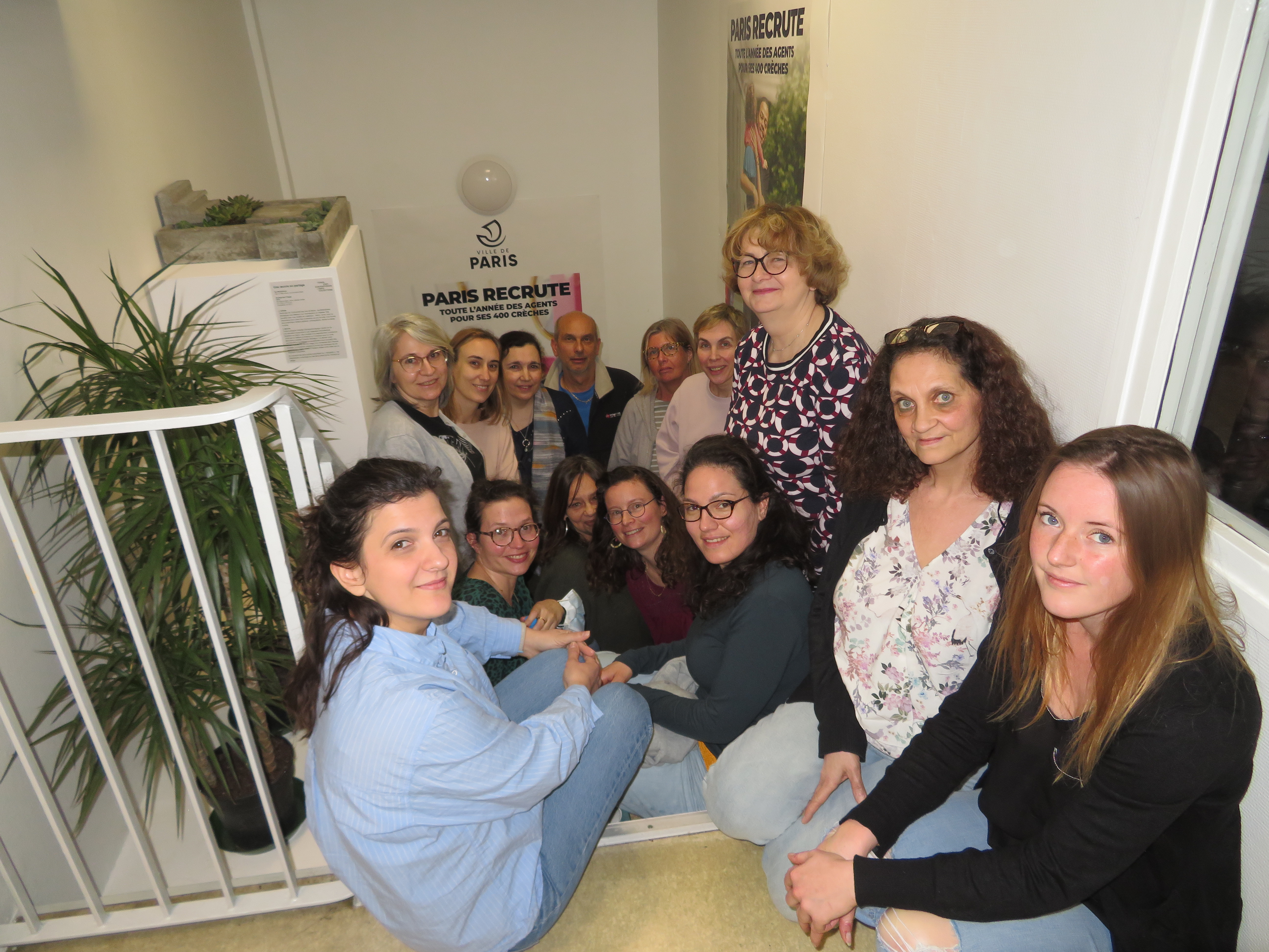 Un groupe d'adulte est assis dans un escalier. Ils se tiennent à proximité d'une oeuvre d'art posée sur un socle et regarde tous l'objectif.