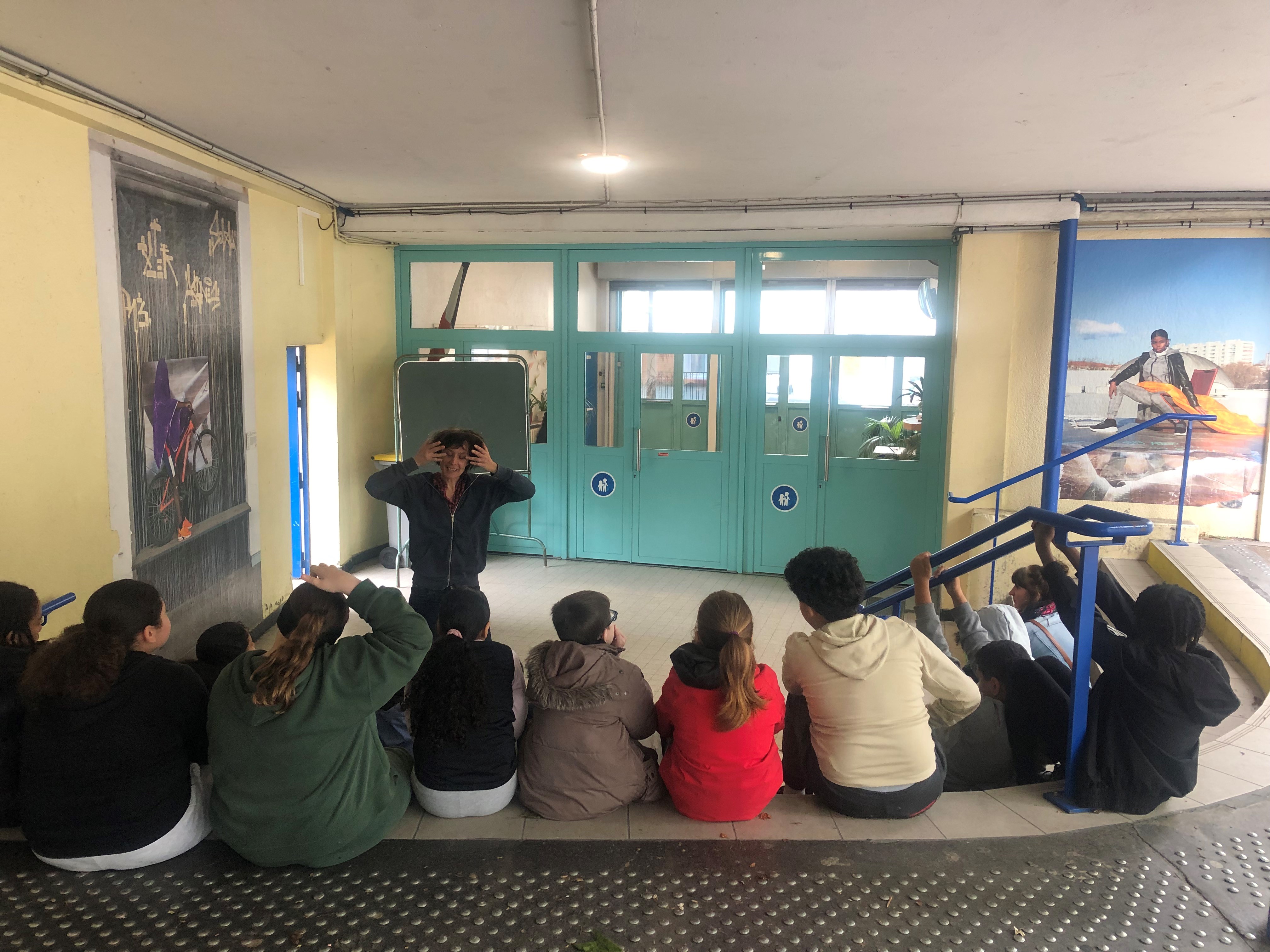Peggy raconte son histoire devant les deux grandes photographies de Melika Shafahi dans une sorte d'atrium. Les élèves l'écoutent assis sur les marches.