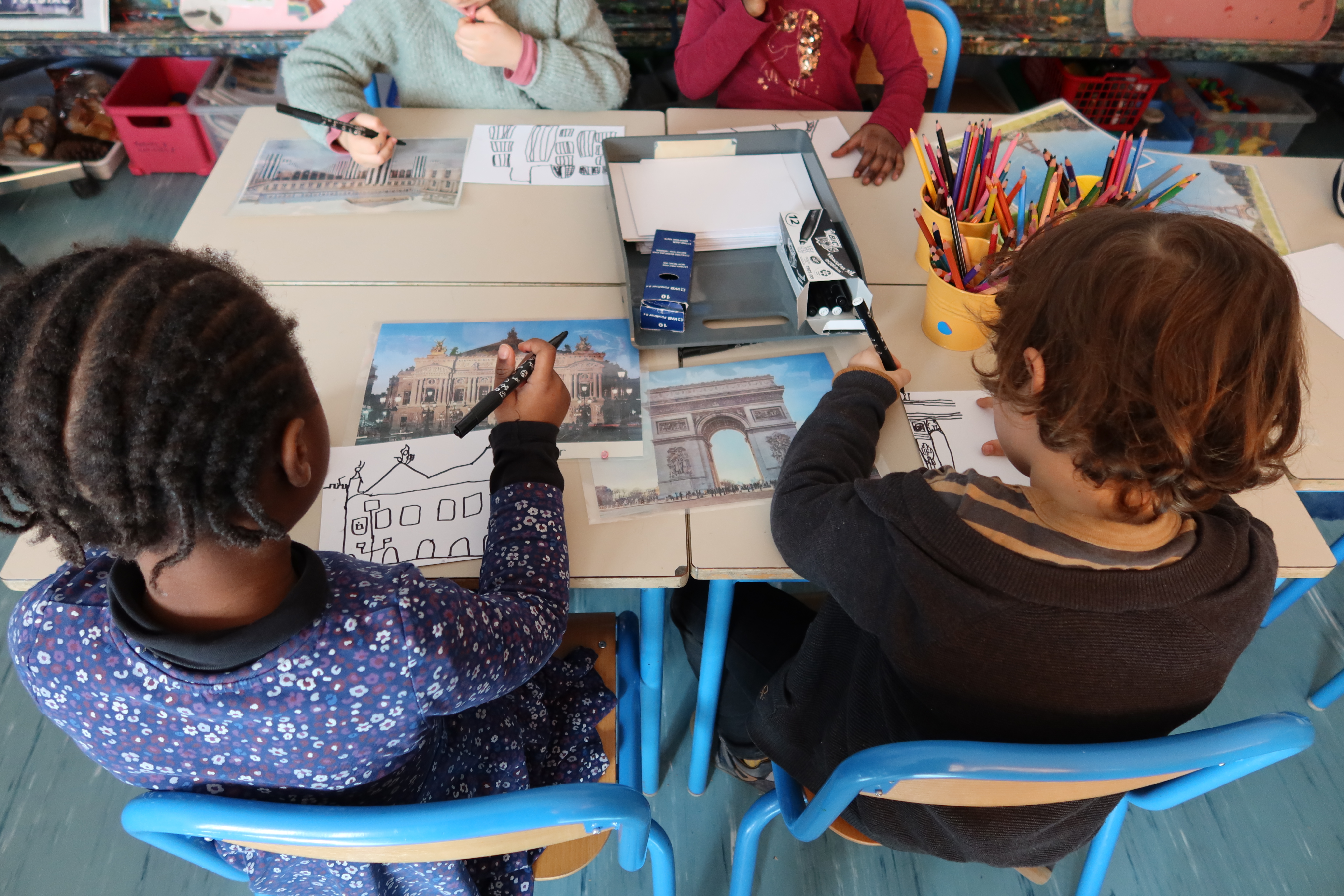 Un groupe d'enfants sont installés autour d'une table. Ils sont en train de redessiner les monuments de Paris d'après photos
