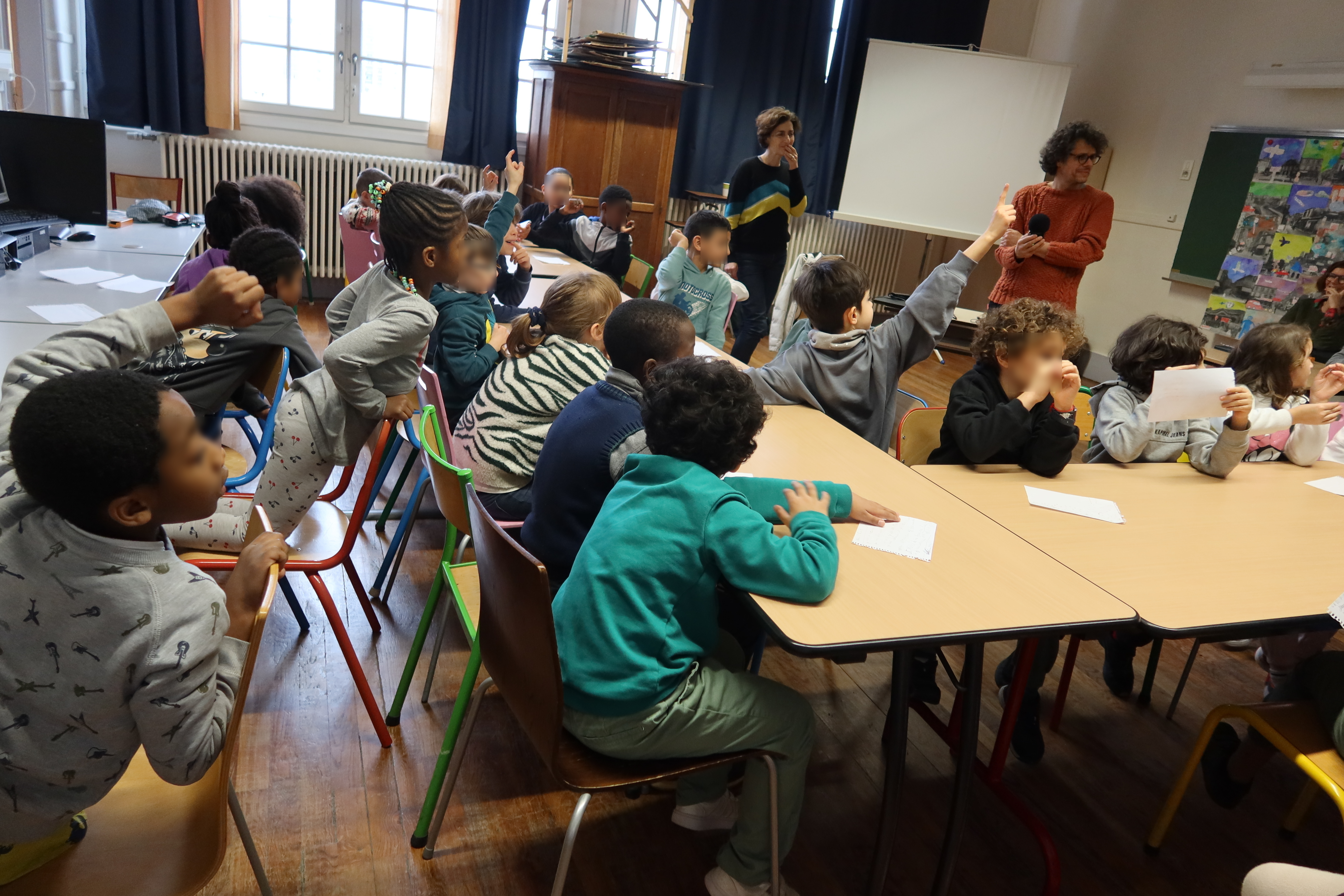 Les enfants assis autour d'une table lèvent le doigt pour pouvoir lire le texte écrit durant l'atelier à leurs camarades.