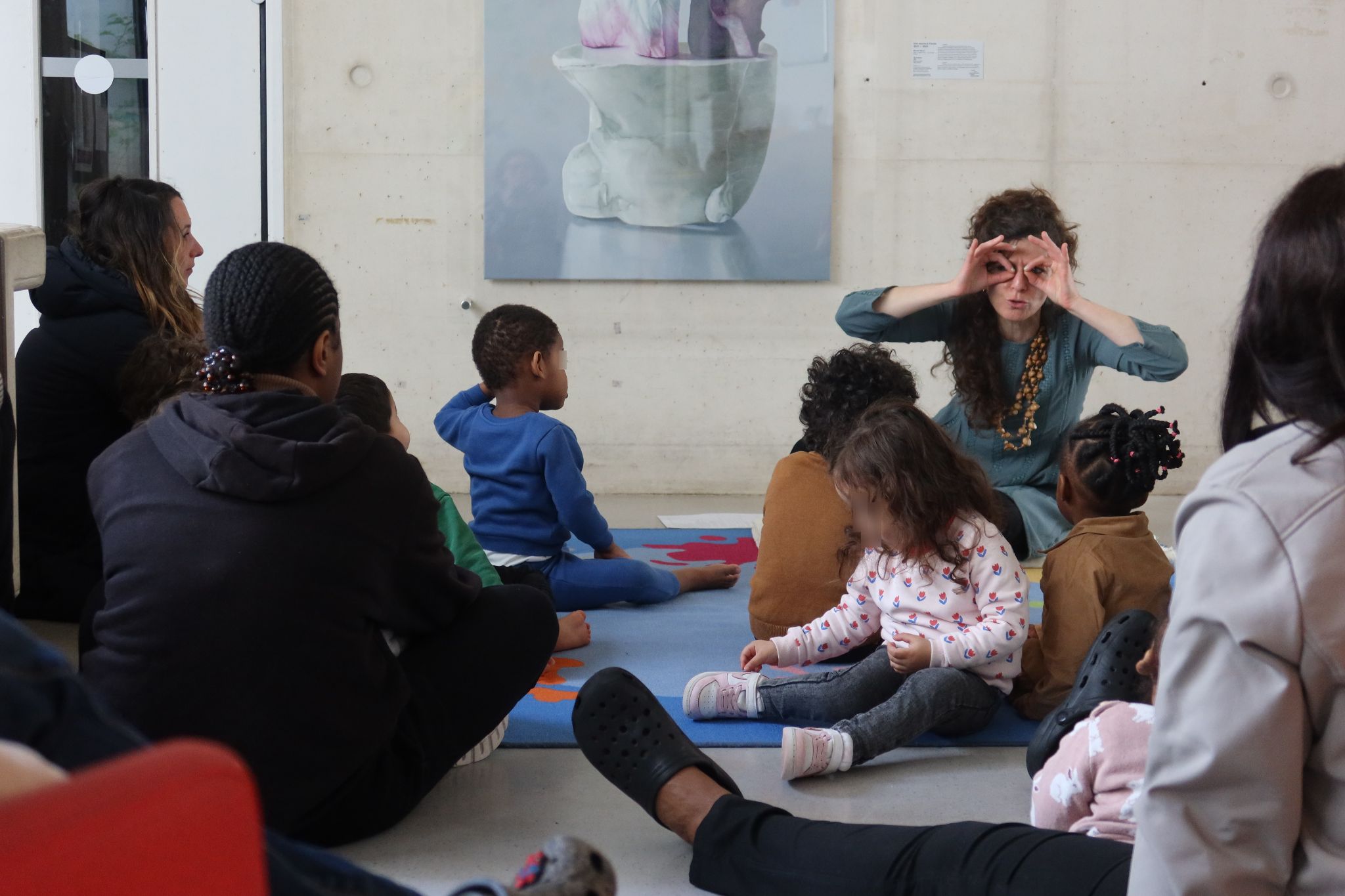 Maïa, la conteuse, est assise au pied du tableau de Maude Maris. En face d'elle sont installés les enfants et les adultes. Alors qu'elle leur raconte son histoire, elle joint le geste à la parole. Les mains vissées en cercle devant ses yeux, elle imite les étranges lunettes d'un hibou