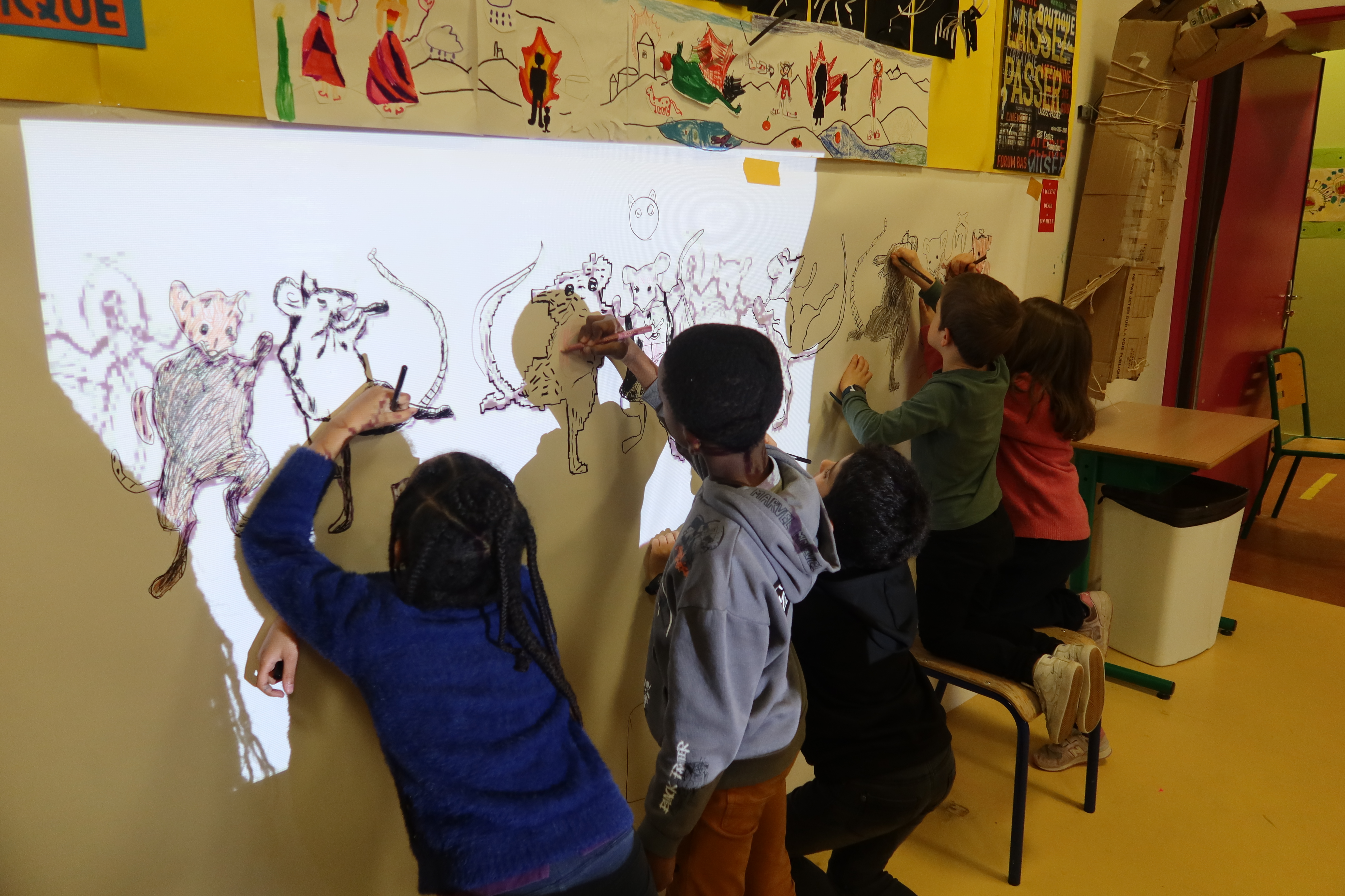 Cinq élèves repassent aux feutres un dessin souris projetées sur le mur de leur salle d'art plastique