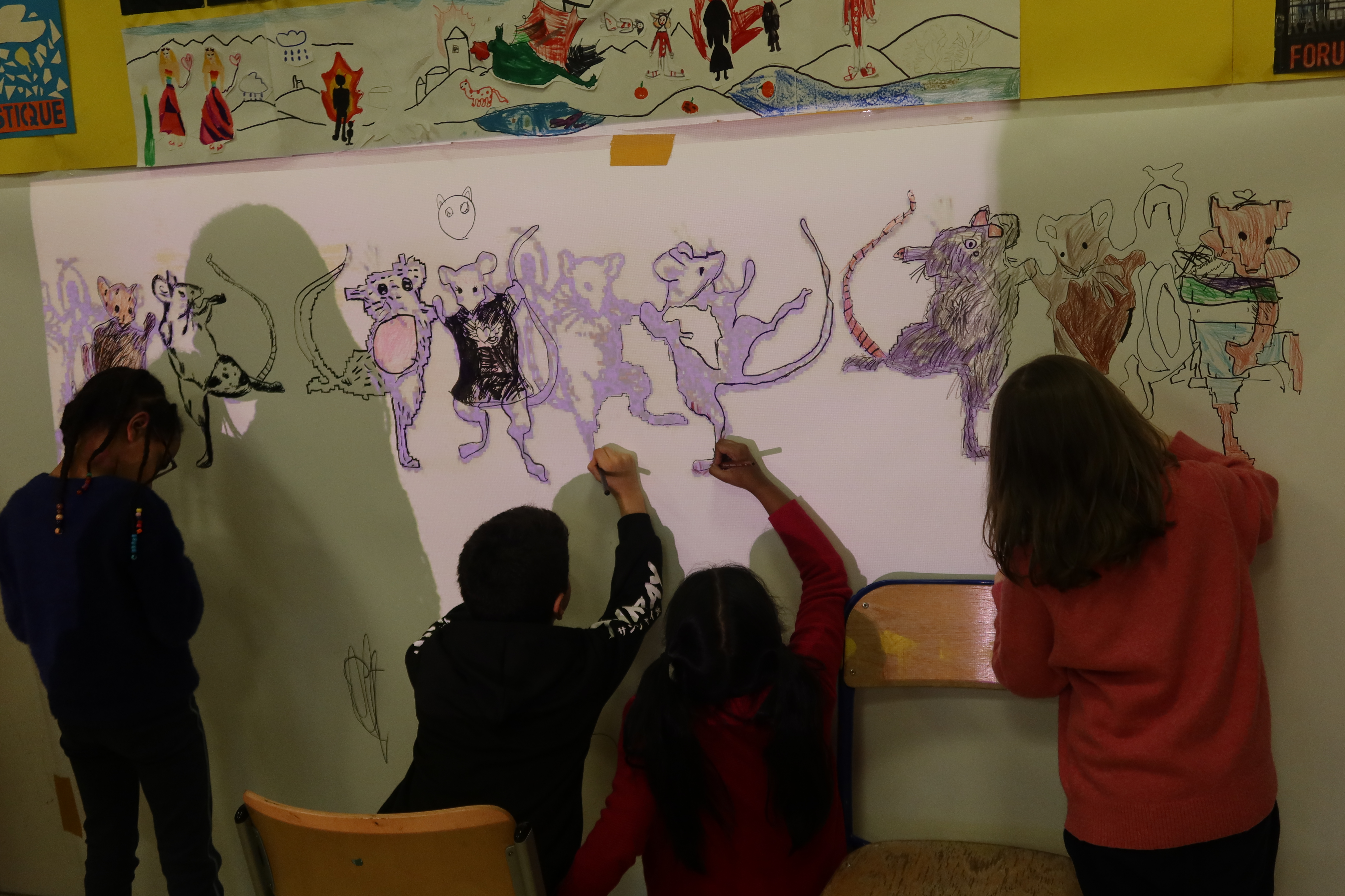 Quatre élèves colorient et habillent les souris qu'ils viennent de décalquer sur une grande feuille fixée au mur de leur salle d'art plastique.
