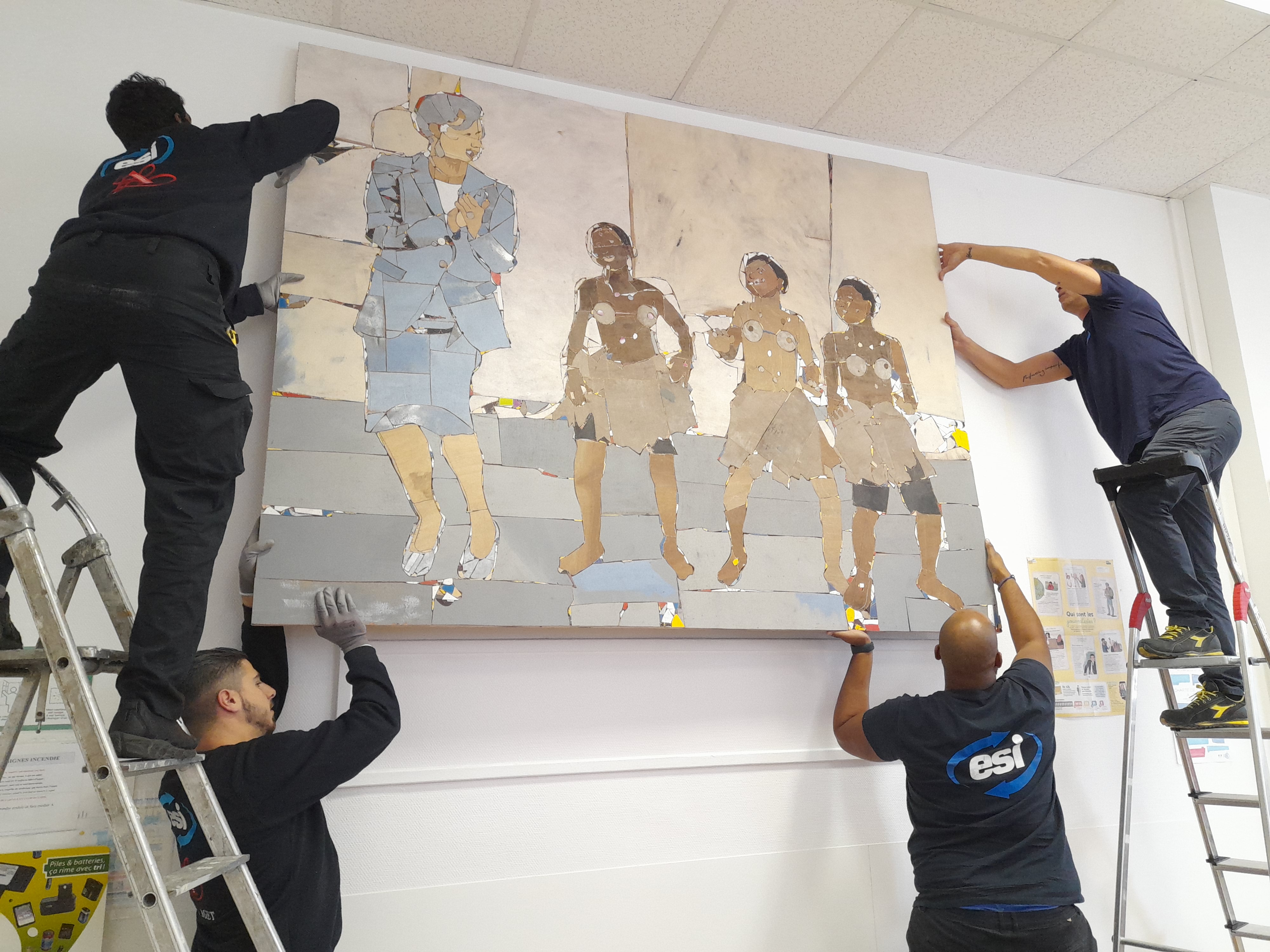 Quatre hommes accrochent un tableau au mur. Deux sont sur une une échelle et deux tiennent le bas du tableau depuis le sol.