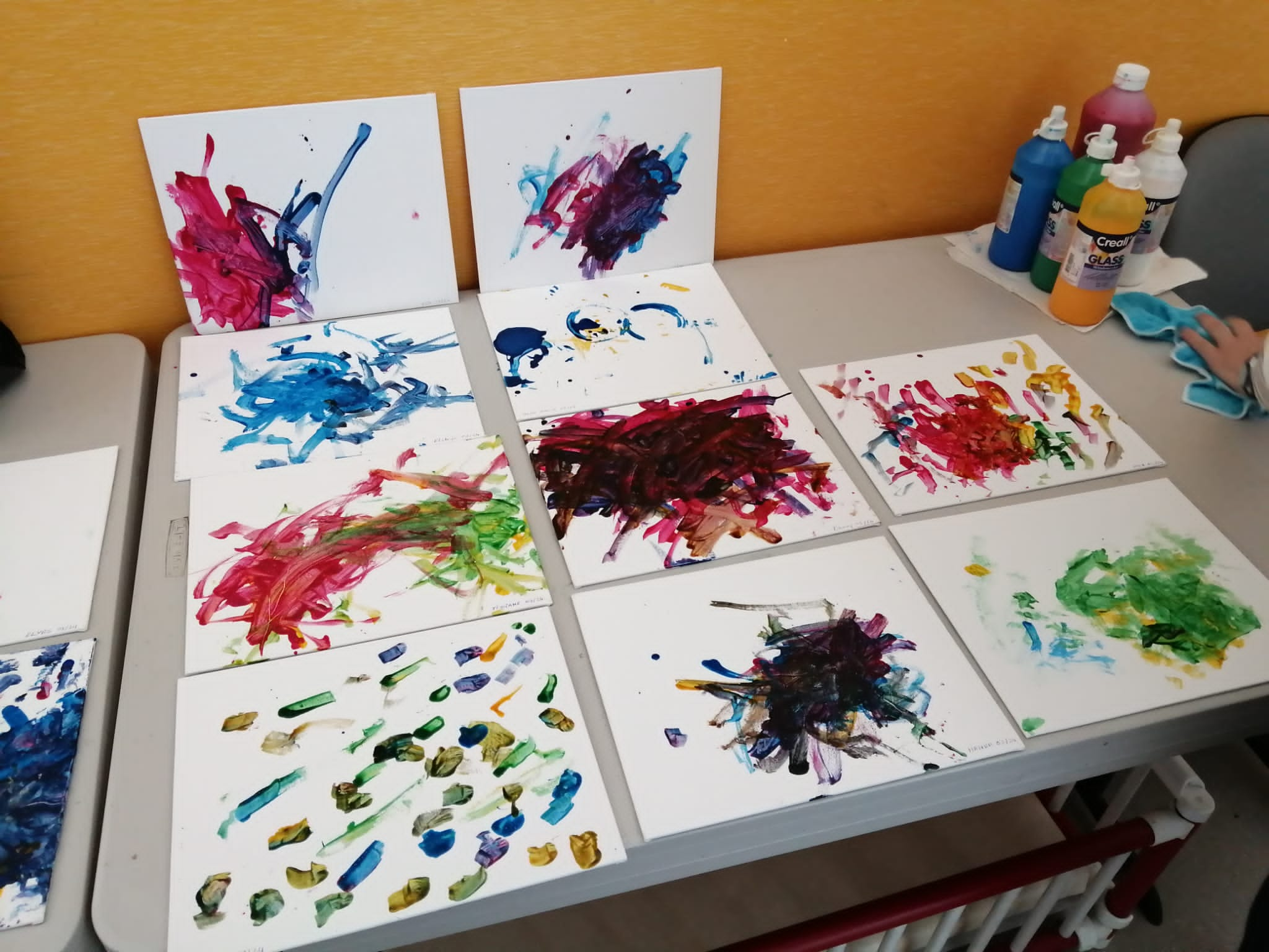 Sur une table sont posées plusieurs peintures d'enfants réalisées sur des feuilles au format A4