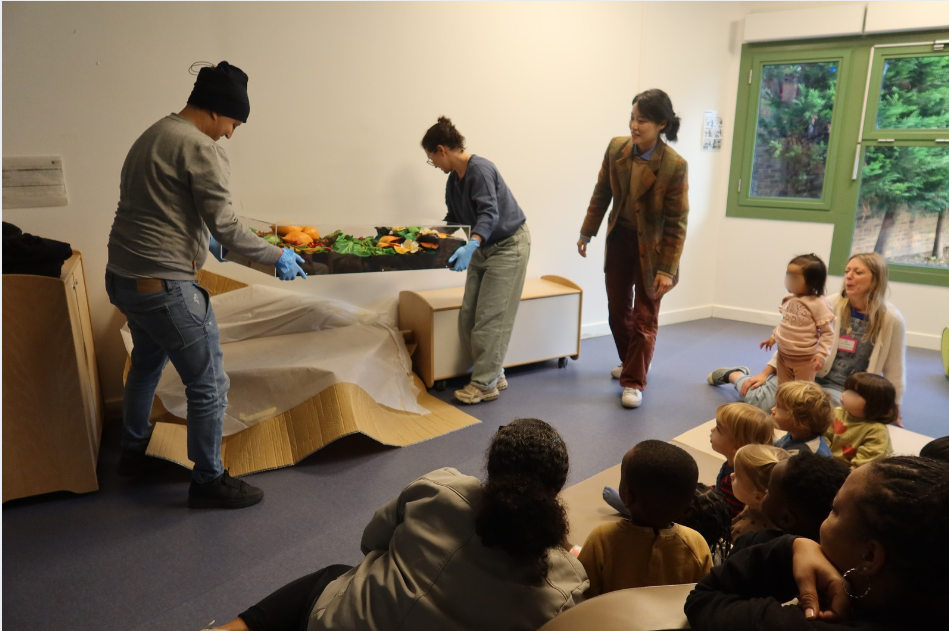 L'installateur-monteur Farid Lmakloufi et la responsable de la régie Julie Degorce déballe la sculpture [Papaya in giardino] de l'artiste Piero Gilardi devant les jeunes enfants et l'équipe de la crèche Buisson St-Louis (10e)