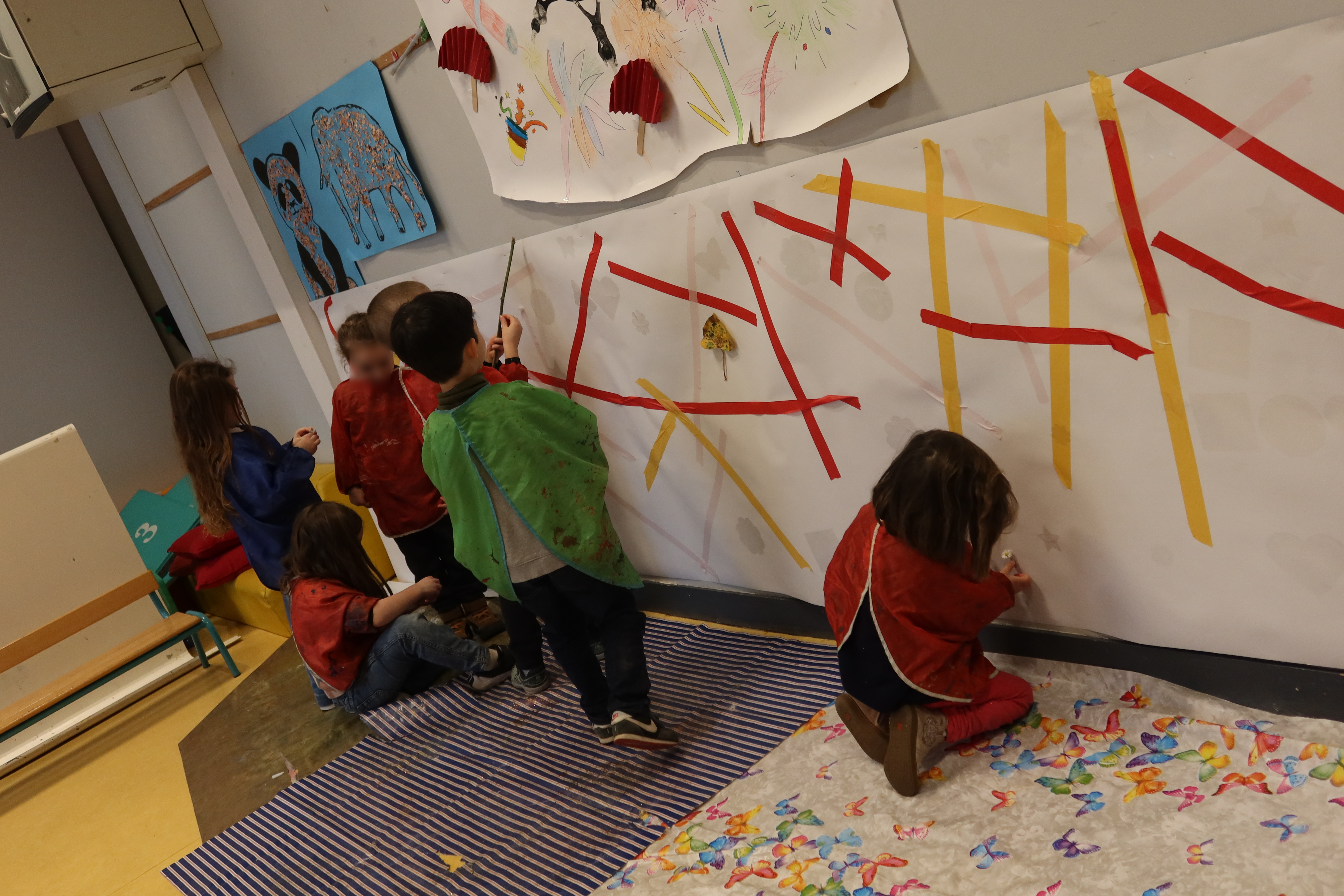 Les enfants collent des bandes de scotch colorées et des formes transparentes sur leur fresque