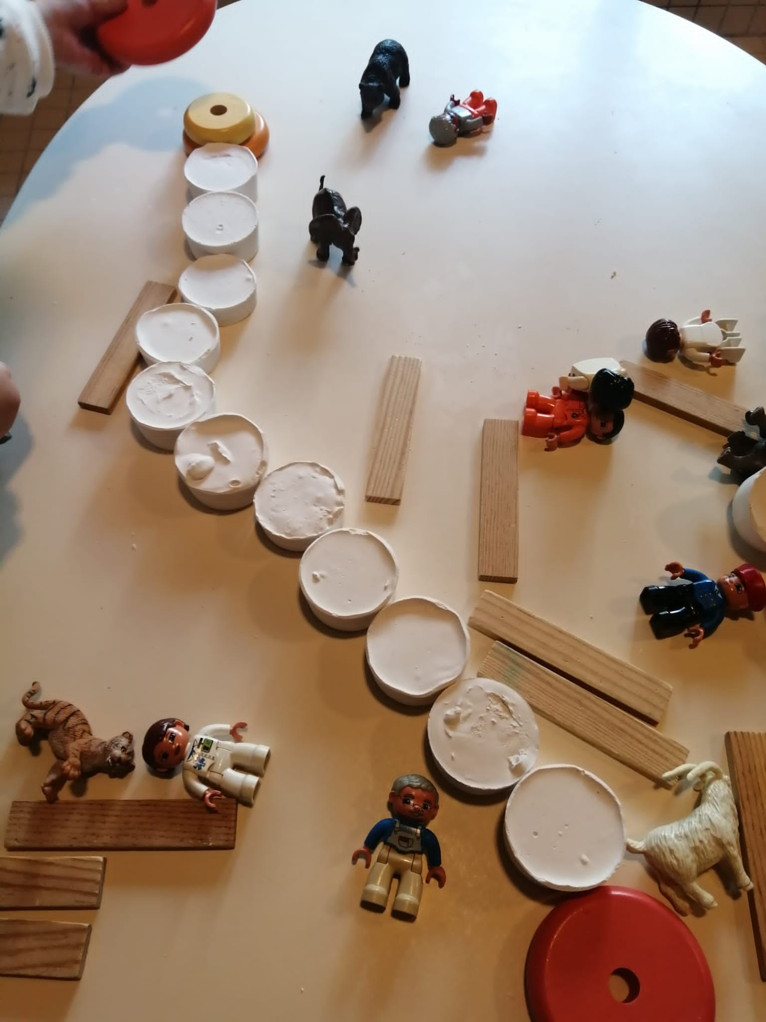 En jouant avec des galets de plâtres, les enfants on réalisé un chemin. Celui-ci est posé sur une table et est entouré de Kapla et de figurines.